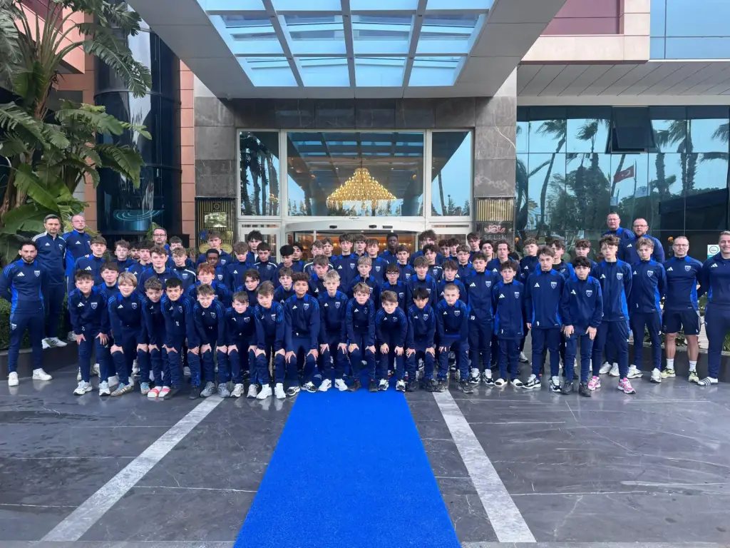 Gruppenfoto: rund fünfzig Jugendspieler und Betreuer in dunkelblauen Kickers-Trainingsanzügen vor einem Hotel